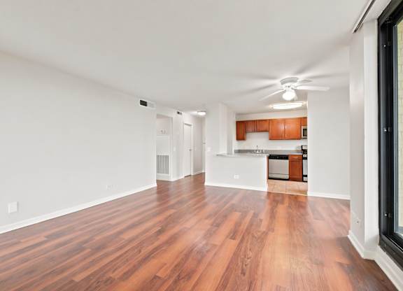 A living room with wooden floors and ceiling fan with the kitchen in the background.