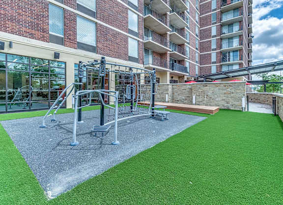 A gym with a green floor and grey equipment is located in front of a brick building.