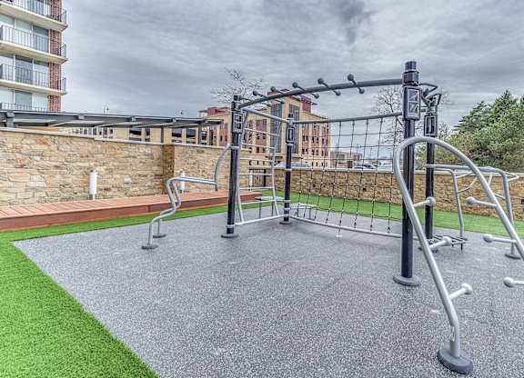 A gym equipment set up on a grey surface with a green grass area and a stone wall in the background.