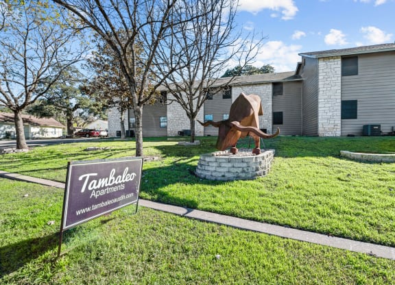 a statue of a bull in the grass in front of a building