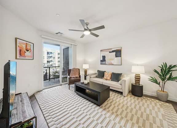 A living room with a white couch, a coffee table, and a ceiling fan.at Fora Apartments, Nevada