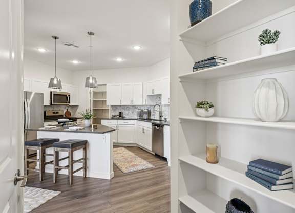 A kitchen with white cabinets and a white island with a bar stool.at Fora Apartments, Las Vegas Nevada