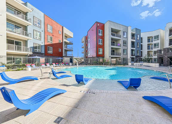 A swimming pool surrounded by blue lounge chairs in front of apartment buildings.at Fora Apartments, Nevada