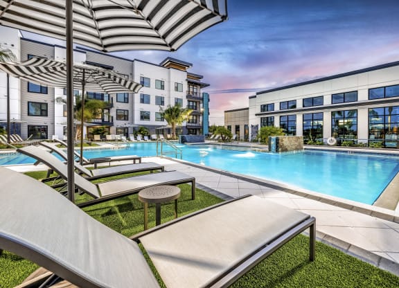 a swimming pool with lounge chairs and umbrellas in front of an apartment building at The Alibi at Lake Lilly, Ocoee