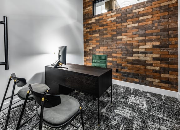 a home office with a desk and chairs and a brick wall