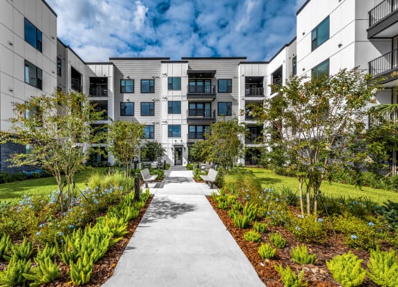 an exterior view of an apartment building with a sidewalk and landscaping at The Alibi at Lake Lilly, Ocoee, FL