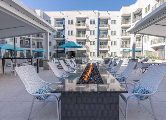 A patio with white chairs and a fire pit in the middle.