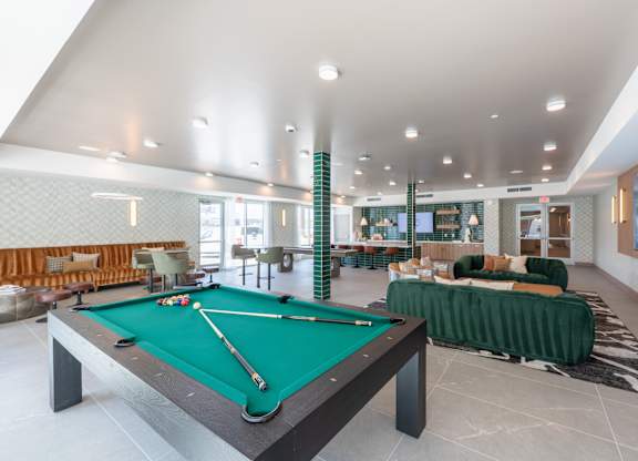 A pool table is in the middle of a room with a green couch.