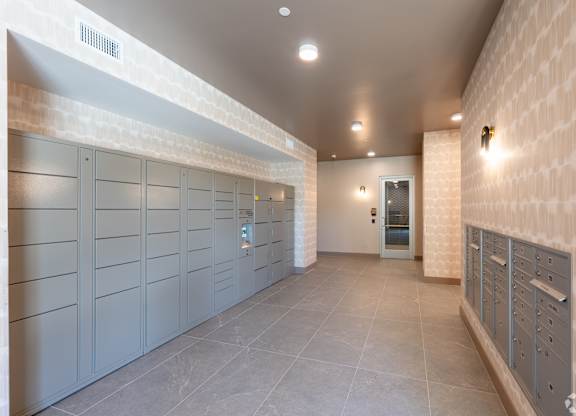 A long hallway with a row of grey lockers on the left and a door at the end.