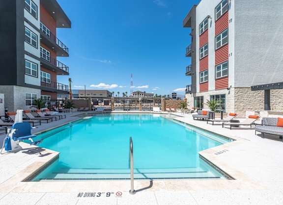 A swimming pool surrounded by lounge chairs and buildings.