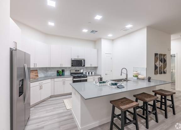 A modern kitchen with a refrigerator, stove, and bar stools.