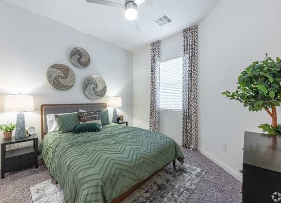 A bedroom with a bed, two lamps, and a plant.