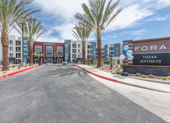 A street view of a Fora Jeffreys apartment complex with palm trees lining the street.