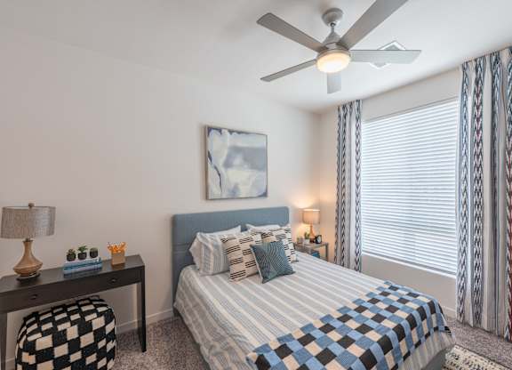 A bedroom with a bed, a ceiling fan, and a window with curtains.
