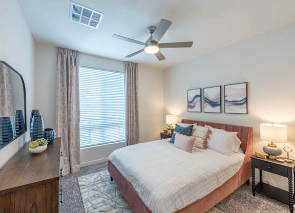 A bedroom with a large bed, a ceiling fan, and a side table with a lamp.