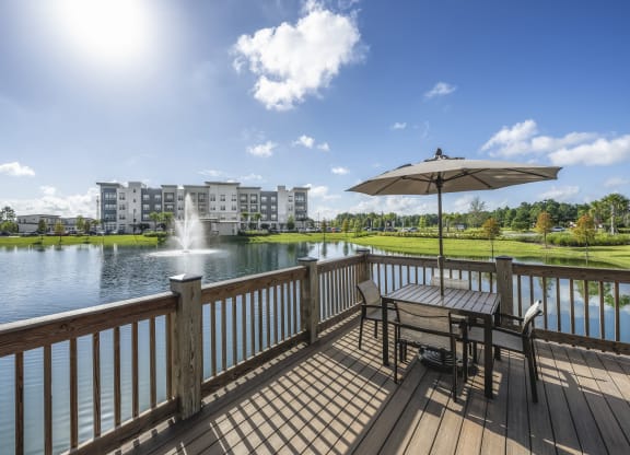 a deck overlooking a lake with a fountain and a table with an umbrella at The Haven at Lake Britt Apartments, Florida, 34787