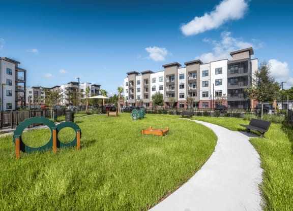 a park with green grass and a path with an apartment building in the background at The Haven at Lake Britt Apartments, Winter Garden, Florida
