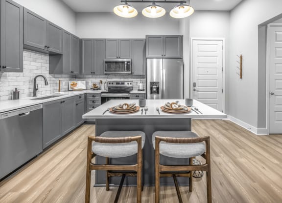 a kitchen with gray cabinets and a island with two chairs at The Haven at Lake Britt Apartments, Winter Garden