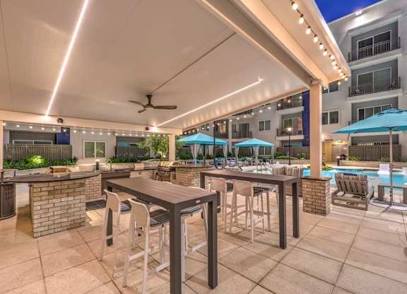 A patio with a bar and chairs is illuminated by overhead lights.