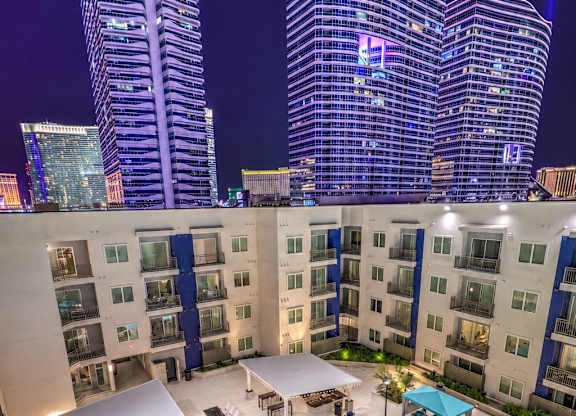 A swimming pool with loungers and umbrellas is surrounded by apartment buildings.