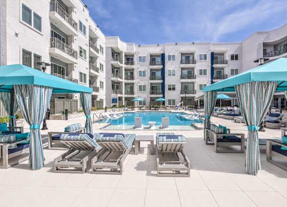 A pool area with lounge chairs and umbrellas in front of a white building.