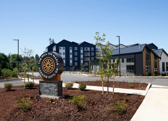a building with a sign in front of it on a sidewalk at The Mill on Maple Apartments, Oregon, 97045