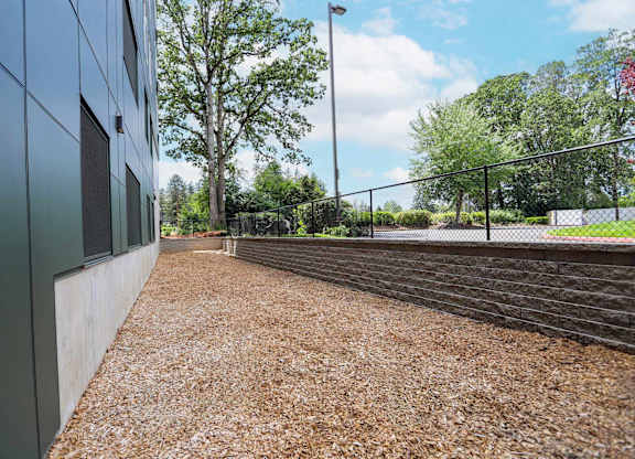 A gravel pathway leads to a fenced area with trees in the background.