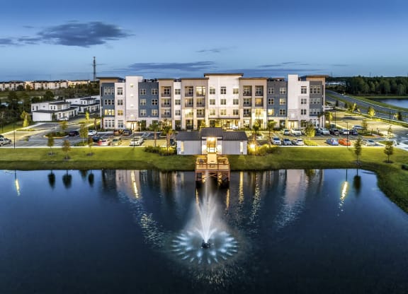 a fountain in the middle of a pond with an apartment building in the background at The Overlook, Winter Garden, 34787