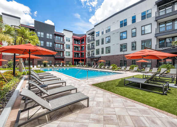 A pool surrounded by chairs and umbrellas with apartment buildings in the background.at Parkway Crossings, Kissimmee, 34744