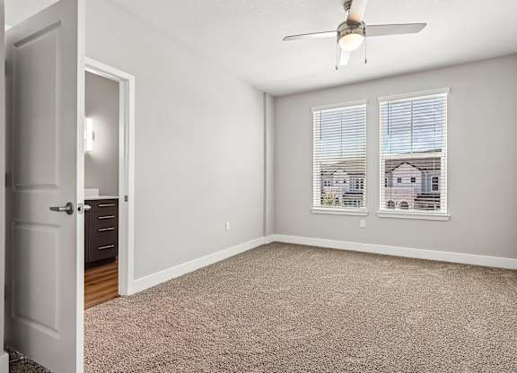 A room with a carpeted floor, a ceiling fan, and a window with blinds.