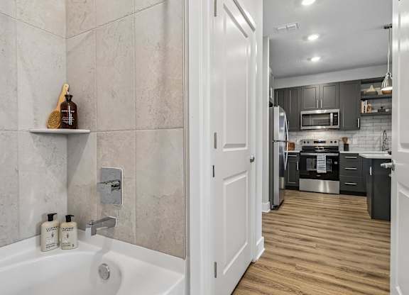 A bathroom with a tub and a kitchen in the background.