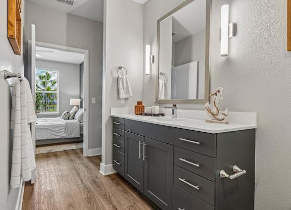 A bathroom with a vanity, mirror, and a bedroom in the background.