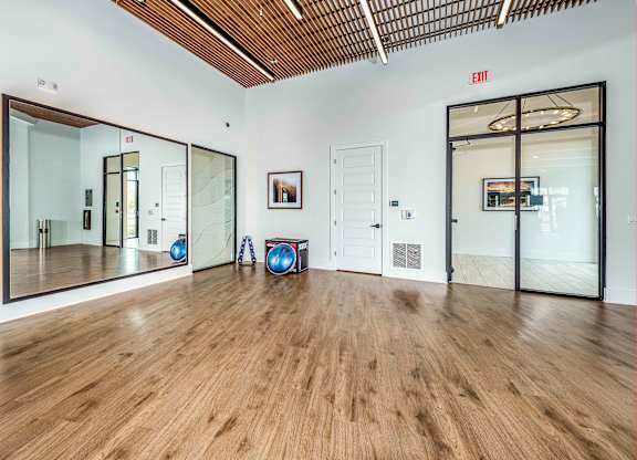 A room with wooden floors and a white wall with a red exit sign.