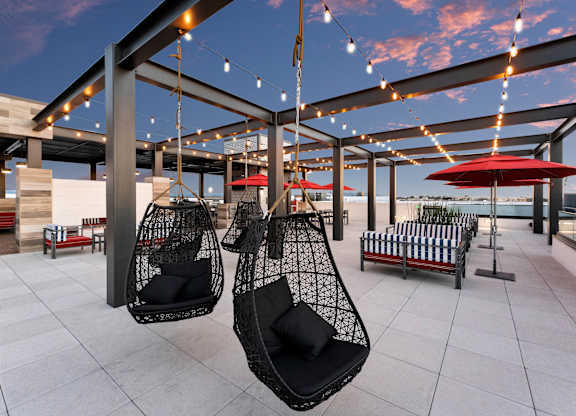 A modern outdoor seating area with hanging chairs and string lights.
