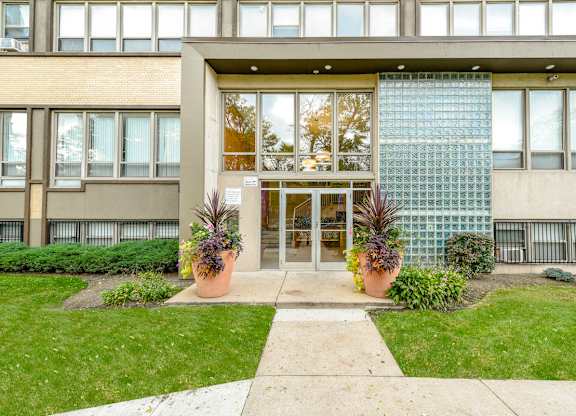 A building with a glass wall and a small garden in front. at Academy at Drexel Apartments, Chicago, 60637