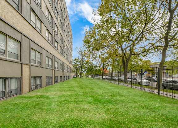 A long grassy area in front of a building with a tree on the right. at Academy at Drexel Apartments, Chicago, Illinois