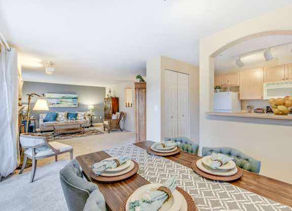 A dining room with a table set for four with a view into the living room and kitchen area at The Lodge at Peasley Canyon in Federal Way, Washington 98001