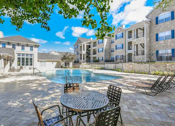 A patio with a table and chairs overlooks a pool.