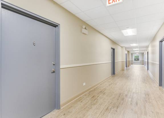 A long hallway with a grey door on the left and a red exit sign on the ceiling. at Academy at Drexel Apartments, Chicago, 60637