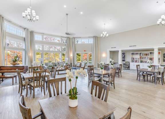 A room with wooden chairs and tables with a vase of flowers on the table in the center at Manor at Victoria Park, Temple Hills, 20748
