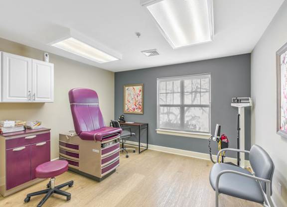 A medical examination room with a purple chair and a grey chair at Manor at Victoria Park, Temple Hills, 20748