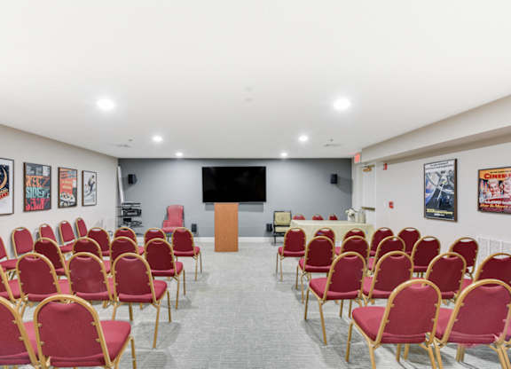 A room with red chairs and a white table with a black screen on the wall at Manor at Victoria Park,  Maryland