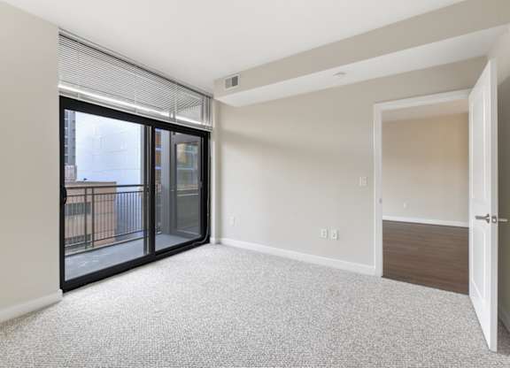 A room with a carpeted floor and a sliding glass door leading to a balcony. at Affinity at 2M, Washington
