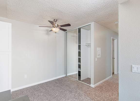 A room with a ceiling fan and a mirrored closet.