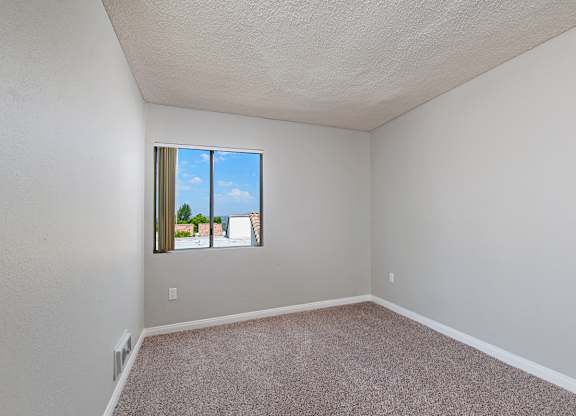 A room with a window showing a view of a building and a blue sky.
