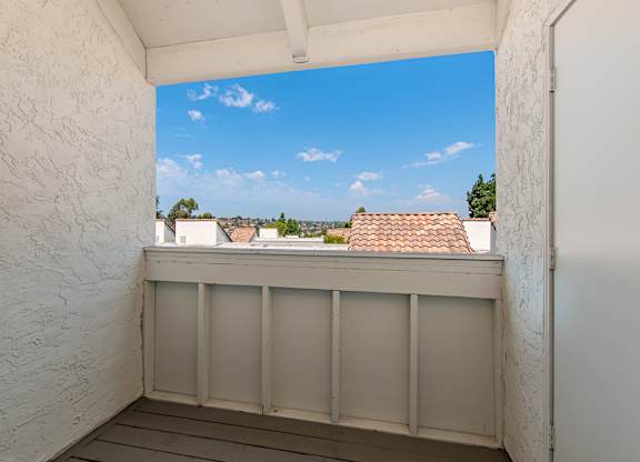 A balcony with a white wall and a view of the sky.