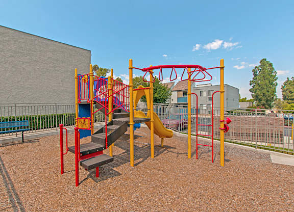 A playground with a red and yellow swing set.