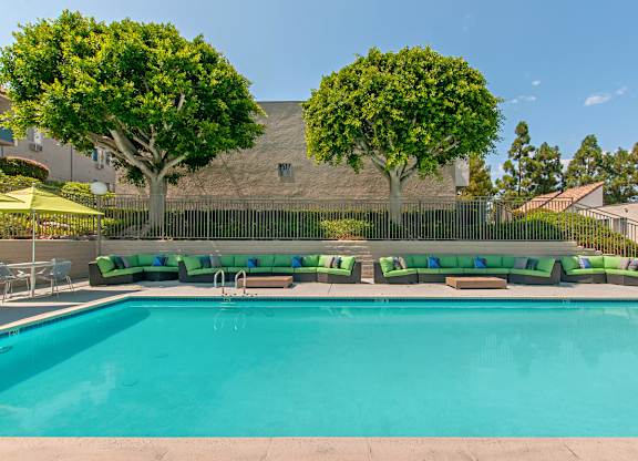 A large swimming pool with a green bench and trees in the background.