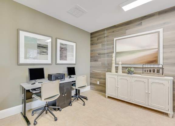 A room with a desk, chairs, and a cabinet with a painting on the wall.