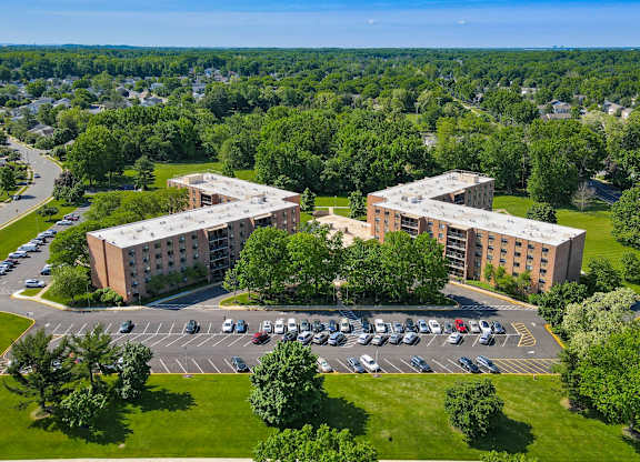 A parking lot in front of a building with a green lawn at Menlo Manor Apartments, Edison, 08820
